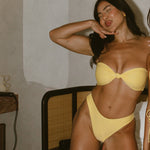 Woman in yellow bikini posing on a bed with a breakfast tray.