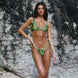 Woman in a green and brown patterned bikini standing against a rocky background