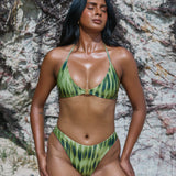 Woman wearing a two tone green patterned bikini against a rocky background