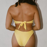 Woman facing away wearing a yellow bikini against a plain background