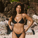 Woman in a black string bikini standing on a rocky beach.